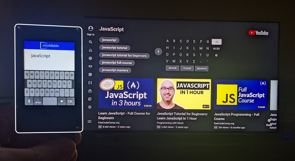 A Moddable Two running a keyboard application, being used to input text to the YouTube app running on a Samsung TV.